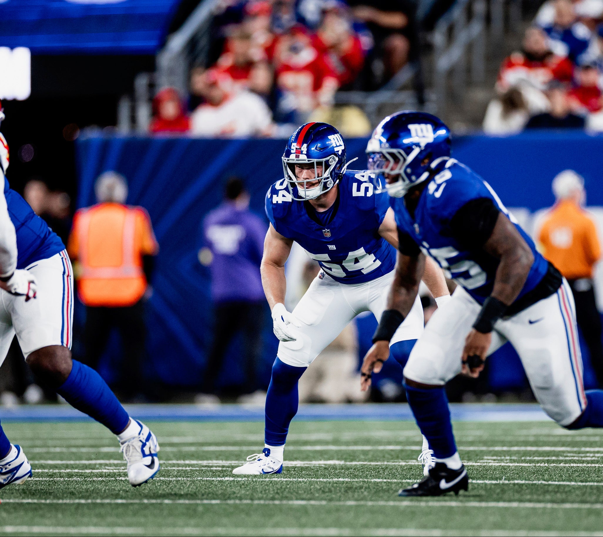 American football players in blue and white uniforms on a field with spectators in the stands.