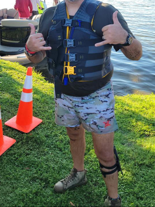 Man in life jacket giving thumbs up by a lake with safety cones and a boat in the background